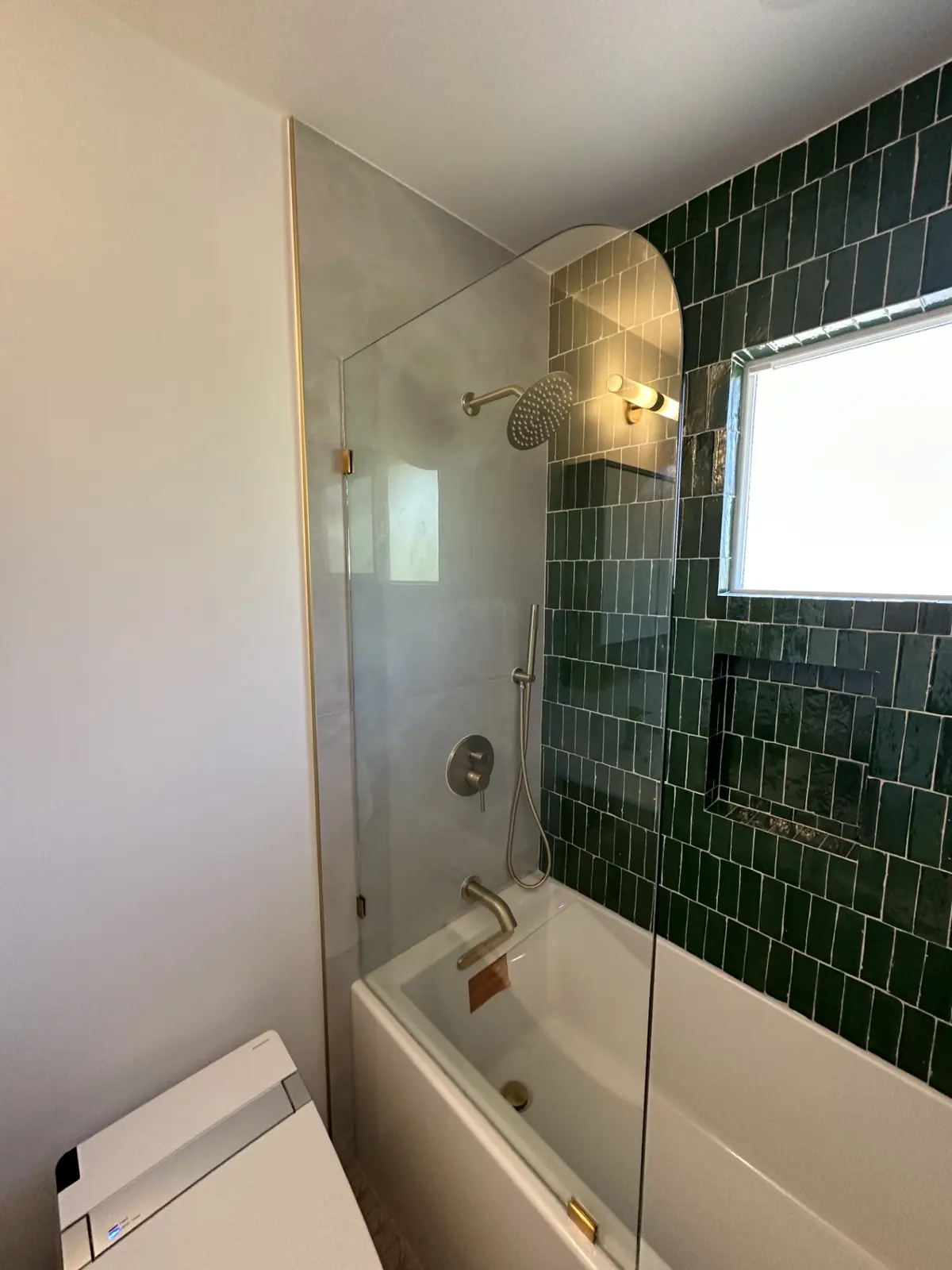 Glass shower with green tile and brass fixtures