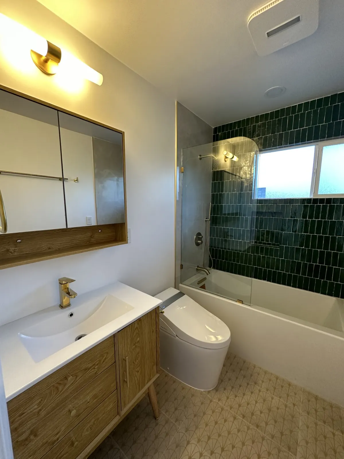 Bathroom with deep green vertical tile, brass fixtures, and a wood vanity