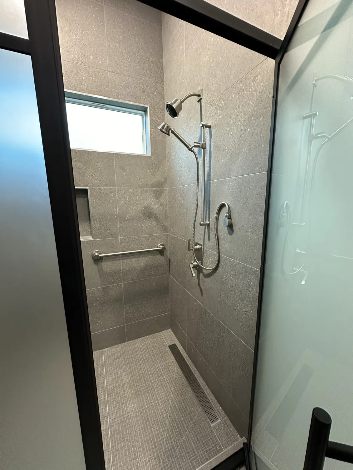 Walk-in shower with gray tile, a built-in bench, and a niche
